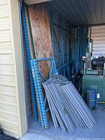Blue steel uprights, plywood sheets, stacked silver support slats inside storage unit