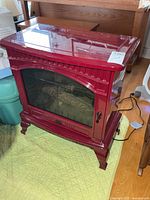 Front view of red stove-style electric fireplace with glass door and power cord visible