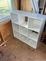 Front view of white 9-cube shelf showing compartments and damaged panel