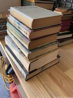 Full stack of eight hardcover books on wooden surface