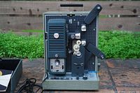 Front view showing speaker grille, control panel, lens, reel arms and film path