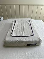 Front view of Purple flat pillow on bed showing cover, piping and logo tag