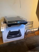 Turntable on top of original box beside metal record rack