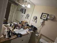 Overview of bathroom counter showing hair dryers, CHI styler box, razor, mirrors, wall art, clock