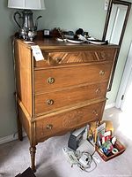 Front view of highboy dresser showing four drawers, legs, hardware, and items atop