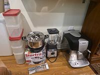Group shot of espresso machine, fondue pot on box, blender, four plastic containers and forks