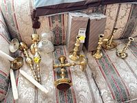 Group view of all brass candlesticks, wall sconces and boxes displayed on sofa