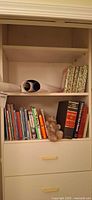 Shelf with two rows of children's books, rolled posters and teddy bear visible