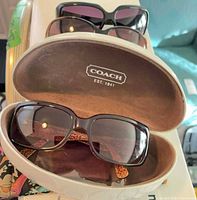 Coach sunglasses in open case with other sunglasses visible behind