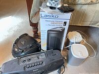 Grouped view showing Lasko heater box, Memorex CD player, Sony radio, two Sonos speakers and remotes