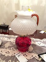 Full view of oil lamp showing milk glass shade, red glass base, chimney