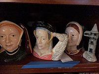 Three Royal Doulton wives character jugs on shelf