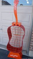 Front view of red guitar-shaped wine rack showing metal grid interior and lettering