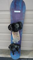 Full view of snowboard with bindings attached, leaning against wall