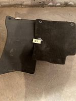 Two of the black carpet mats showing shape and grommet holes