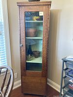 Full view of tall narrow cabinet with glass door and wood panel base