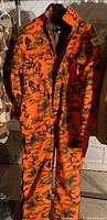 Front view of full jumpsuit hanging, showing blaze orange camo pattern and size
