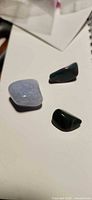 Three tumbled stones on tabletop: pale blue, dark green, green with red flecks