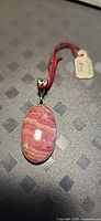Front view of oval rhodochrosite pendant with bail and measurement tag