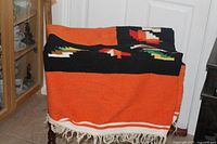 Blanket draped over chair showing orange field, black border, geometric pattern, fringe
