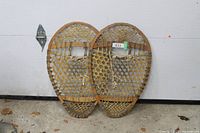 Front view of both wooden bear paw snowshoes leaning together