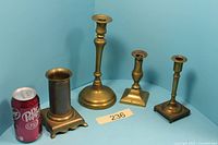Front view of all four brass candlesticks with soda can for scale
