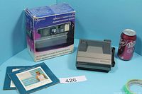 Camera with box, booklets, soda can for scale