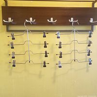 Two chrome metal vertical pant hangers with clips displayed on wall rack