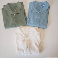 Three folded polo shirts in green, blue and white