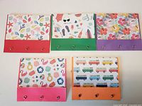 Five mini notebooks closed showing patterned covers and colored flaps with brads