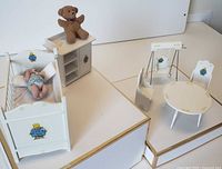 Full view of crib with baby, cabinet with teddy, swing, table and chair