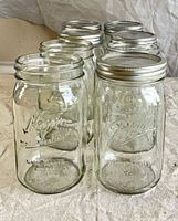 Seven clear glass Mason jars, Ball logo visible, metal lids attached or nearby