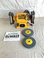 Front view of DeWalt DW756 bench grinder with cord, two loose wheels, manual
