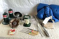 Overview of lantern, stove, propane canisters, fish grill, skewers, tongs and sleeping bag