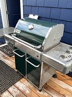 Front angled view of Weber Genesis grill showing green hood, temperature gauge, stainless body, side shelf and cabinet doors