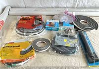 Lot overview showing vinyl rolls, weatherstrip coils, caulking cord boxes and storm door closer