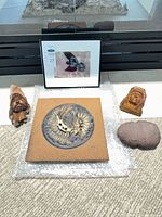 Group shot with all five items: stone hammer, two wood carvings, ceramic plaque, framed crow photo