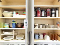Full cupboard view showing plates, bowls, mugs, glasses and travel mugs