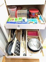 Drawer showing fry pans, sauté pan with lid, muffin tin, storage containers