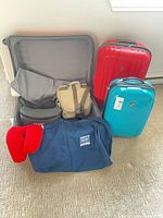 Group shot of open grey suitcase, red and turquoise suitcases, garment bag, crossbody bag, pouch, neck pillow