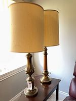 Both brass and wood column table lamps with shades displayed side by side