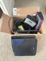 Box with CD wallets and bundled AV cables, large black/blue CD binder on floor
