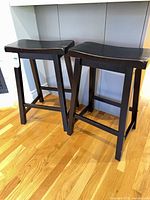 Two black wooden counter stools positioned under counter