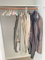 Closet view showing eight beige/khaki and one dark jacket on hangers