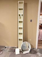 Full view of tall white shelf with round mirror and mirror stand at base