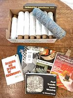 Box containing white cotton spools, blue variegated spool and stack of weaving books