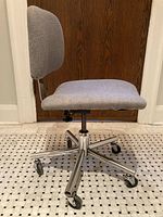 Profile view of grey upholstered swivel desk chair on chrome base with casters