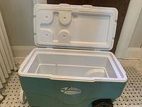 Open Coleman teal hard cooler showing interior and lid hinge