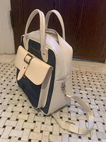 Three-quarter view showing front pocket, top handles, shoulder strap