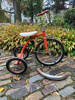 Side view of red CCM tricycle with detached front fender on ground